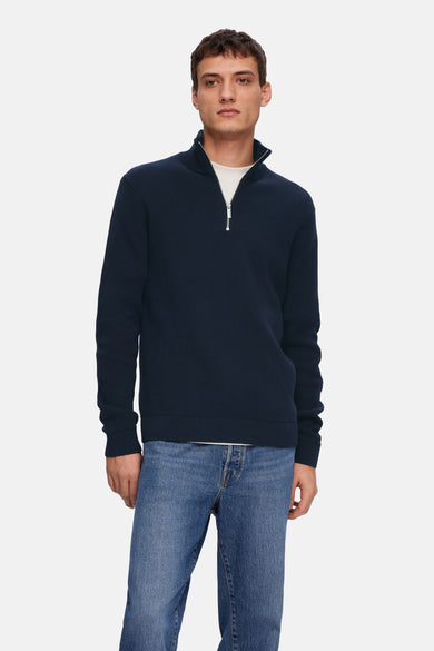 T-shirt bleu de SELECTED, avec une fermeture éclair et porté sur un T-shirt blanc et un jeans bleu.