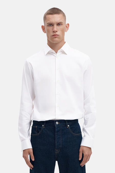 Chemise blanche à manches longues de SELECTED, portée avec un pantalon foncé, les mains dans les poches.