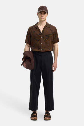 Chemise brune à manches courtes de SELECTED, avec motif feuille, portée avec une casquette brune et un pantalon noir.