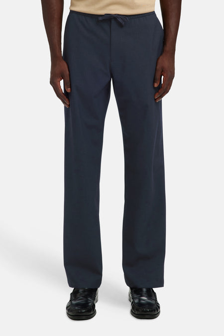 Donkerblauwe broek met elastische taille van SELECTED, rechte pasvorm, voorzien van trekkoord, gedragen met beige trui en zwarte loafers, front view.