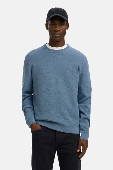 T-shirt bleu avec col rond de SELECTED, en fine texture tricotée et associé à un jean noir et un chapeau.
