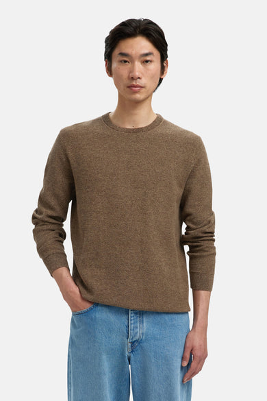 Pull marron avec col rond de SELECTED, porté avec un jean bleu et une main dans la poche.