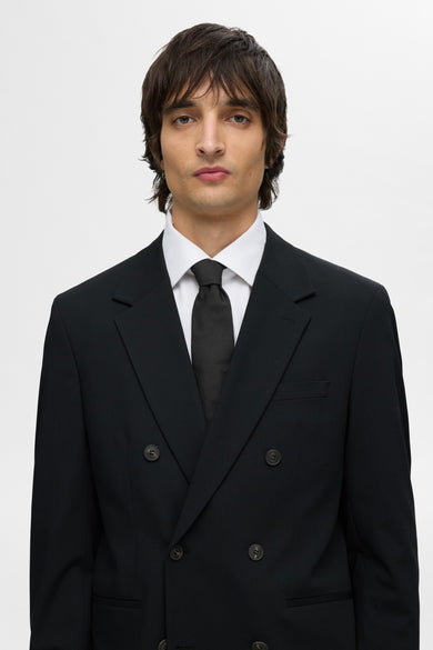 T-shirt noir de SELECTED, porté avec un chemisier blanc et un costume noir à double boutonnage.