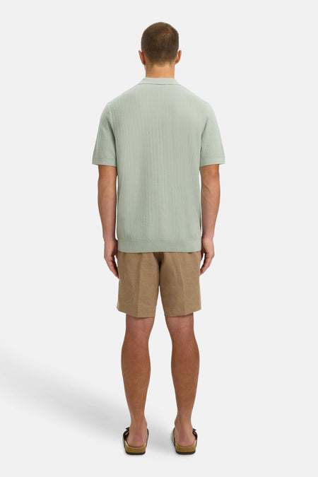 Polo verte SELECTED de couleur verte avec un motif à fines rayures, portée avec un short marron et des sandales.