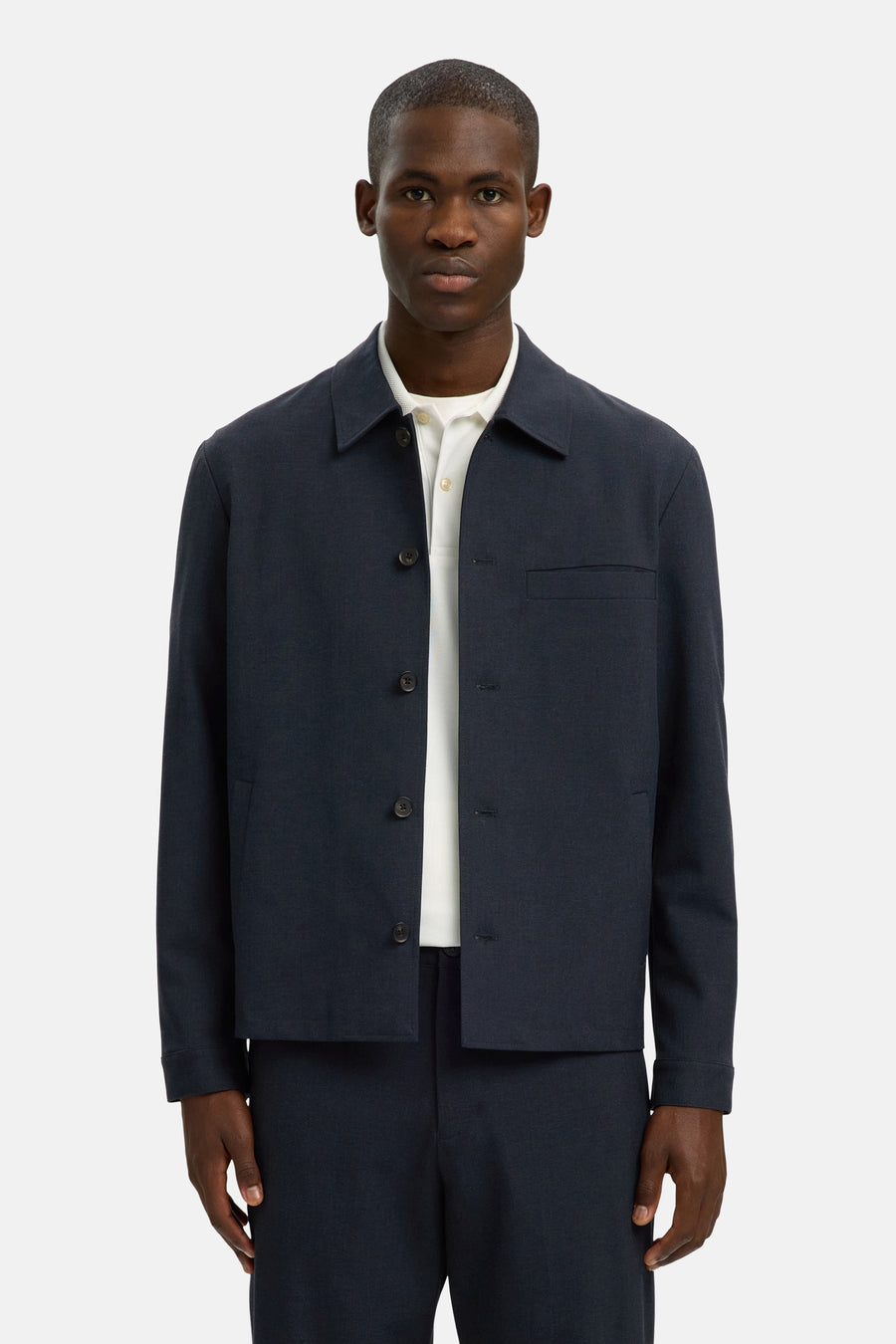 Chemise bleue à manches longues de SELECTED, avec une fermeture boutonnée et une poche poitrine, portée sur un polo blanc et un pantalon bleu foncé.