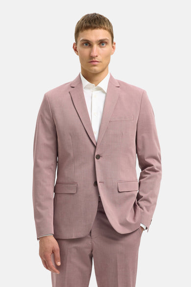 Man in roze pak en wit overhemd, hand in zak.
