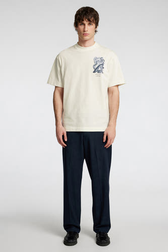 Ecru T-shirt met korte mouwen van SELECTED, met een abstracte grafische print op de borst, gecombineerd met een donkerblauwe pantalon en zwarte loafers.