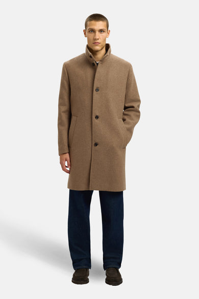 Manteau brun long de SELECTED, avec fermeture à boutons et poches, associé à un jeans bleu foncé et des chaussures brunes.