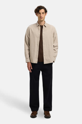 Chemise beige à longues manches de SELECTED, portée sur une chemise brune, avec un pantalon foncé et des chaussures brunes.