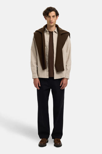 Chemise beige à longues manches de SELECTED, avec une veste brune posée nonchalamment sur les épaules et un pantalon noir.