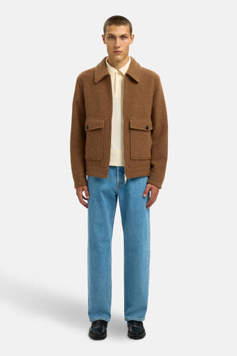 Manteau court brun de SELECTED, avec des poches brodées et porté sur une polo crème et des jeans bleus.