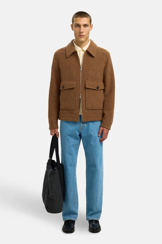 Manteau brun court de SELECTED, avec des poches brodées, associé à un shirt crème, des jeans bleus et une sacoche noire.