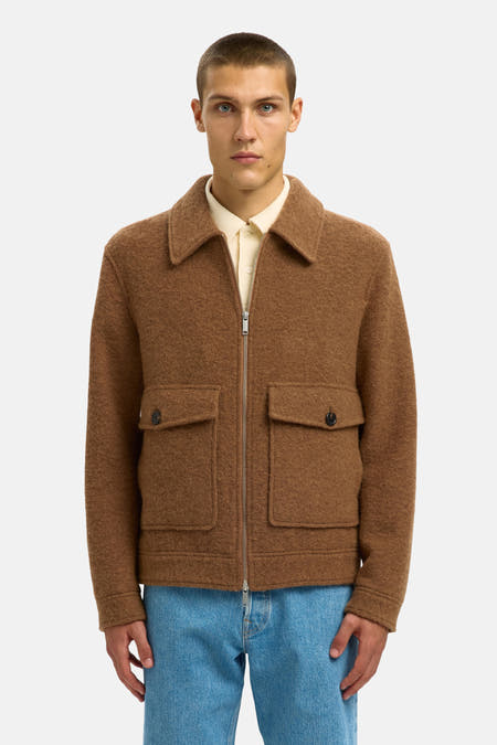 Manteau brun court de SELECTED, avec fermeture éclair et poches brodées, porté sur une polo claire et des jeans bleus.