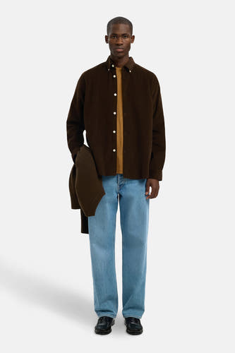 Chemise brune à longues manches de SELECTED, avec une veste brune dans la main et des jeans bleu clair.