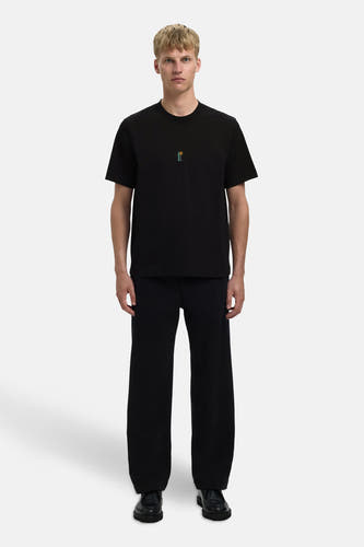 T-shirt noir à manches courtes de SELECTED, avec une petite image brodée et associé à un pantalon noir large et des chaussures noires.