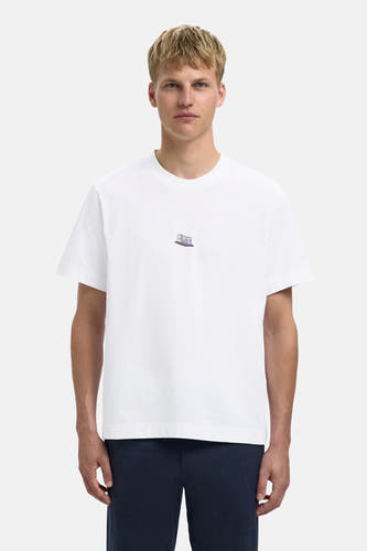 T-shirt blanc à manches courtes de SELECTED, avec une petite impression sur la poitrine, porté avec un pantalon bleu marine.