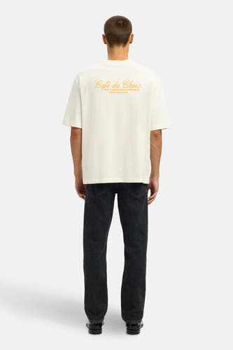 T-shirt écru à manches courtes de SELECTED, avec une impression graphique sur le dos, porté avec des jeans foncés et des chaussures noires.