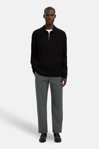 Pull noir avec col rond de SELECTED, porté sur un T-shirt blanc et un pantalon gris avec des chaussures noires.