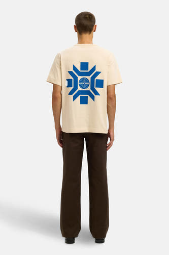 T-shirt beige à manches courtes de SELECTED, avec imprimé bleu sur le dos, associé à un pantalon marron.