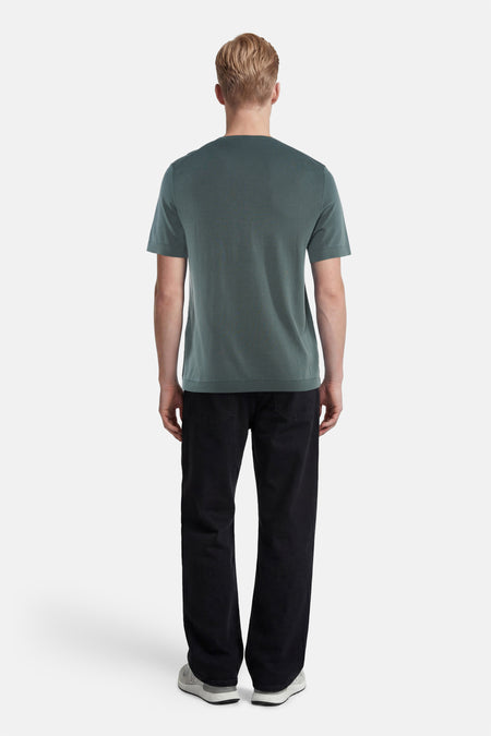 Groene pull met ronde hals van SELECTED, met korte mouwen, van achteren gefotografeerd, gedragen met zwarte broek en grijze sneakers.