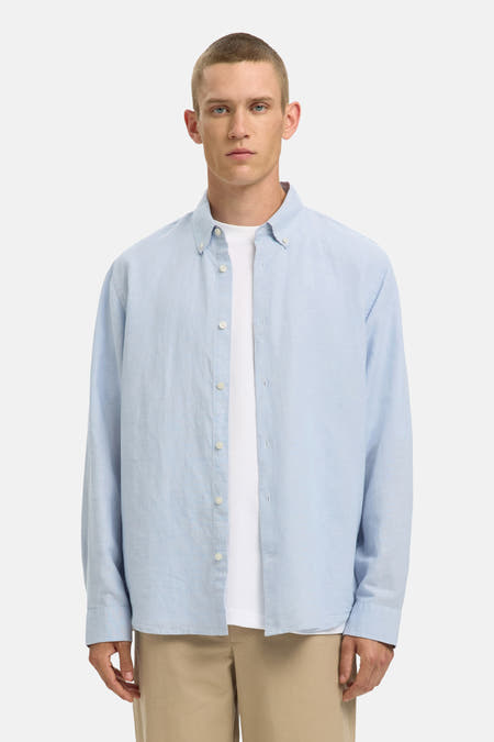 Chemise bleue à manches longues de SELECTED, portée sur un t-shirt blanc, avec un pantalon beige et des mocassins en cuir.