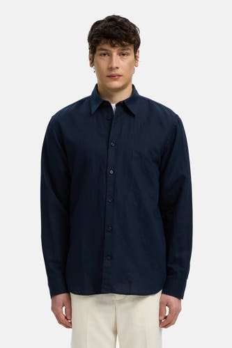 Chemise bleue à manches longues de SELECTED, avec col et boutons, portée par un mannequin sur un t-shirt blanc et un pantalon clair.