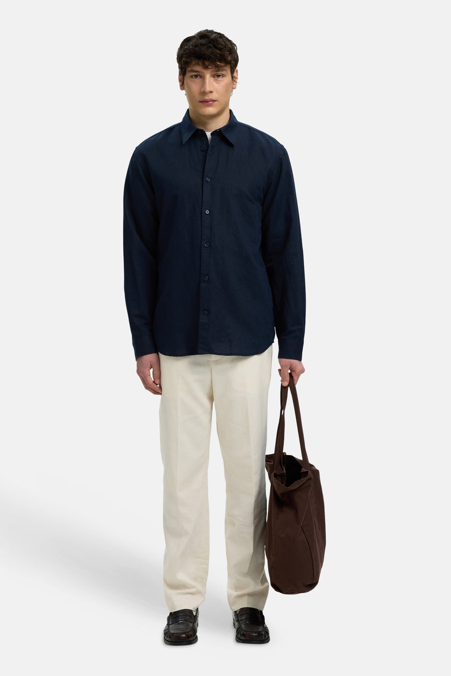Chemise bleue à manches longues de SELECTED, portée par un homme avec un pantalon crème et un tote bag marron.