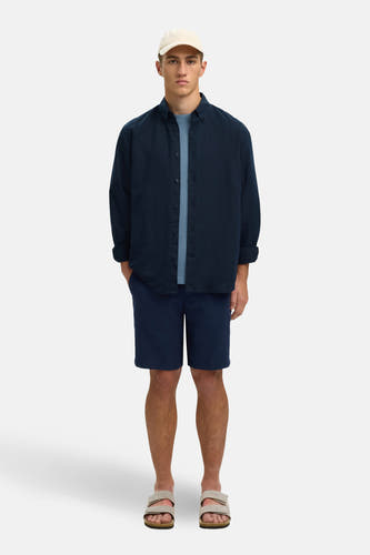 Blauw overhemd met lange mouwen van SELECTED, gedragen over een blauw T-shirt met blauwe shorts en sandalen.