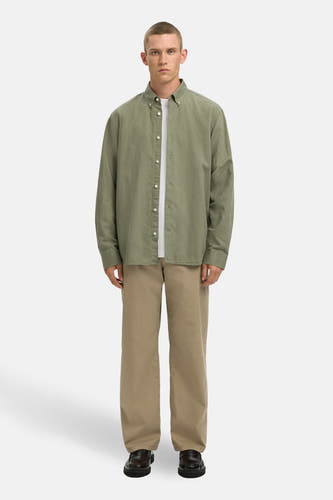 Chemise verte à manches longues de SELECTED, avec fermeture à boutons blanche, portée sur un t-shirt blanc et un pantalon beige.