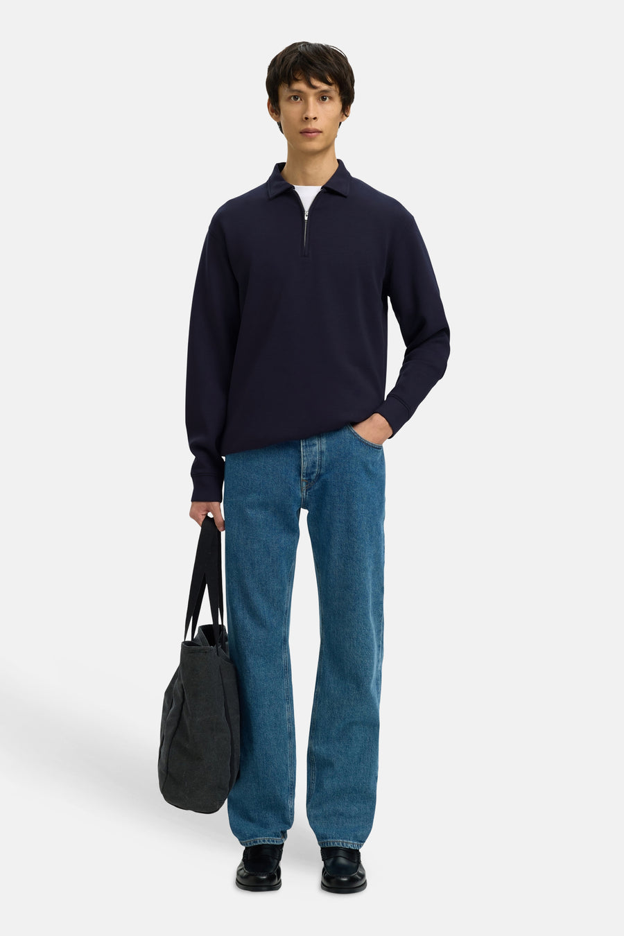 Pull bleu de SELECTED, avec une fermeture éclair et porté avec un t-shirt blanc, un jean et un sac noir.
