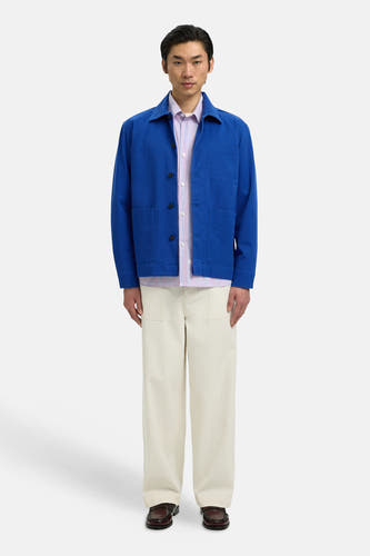 Blauwe jas van SELECTED, gedragen over een gestreept overhemd en crèmekleurige broek, met bruine schoenen.