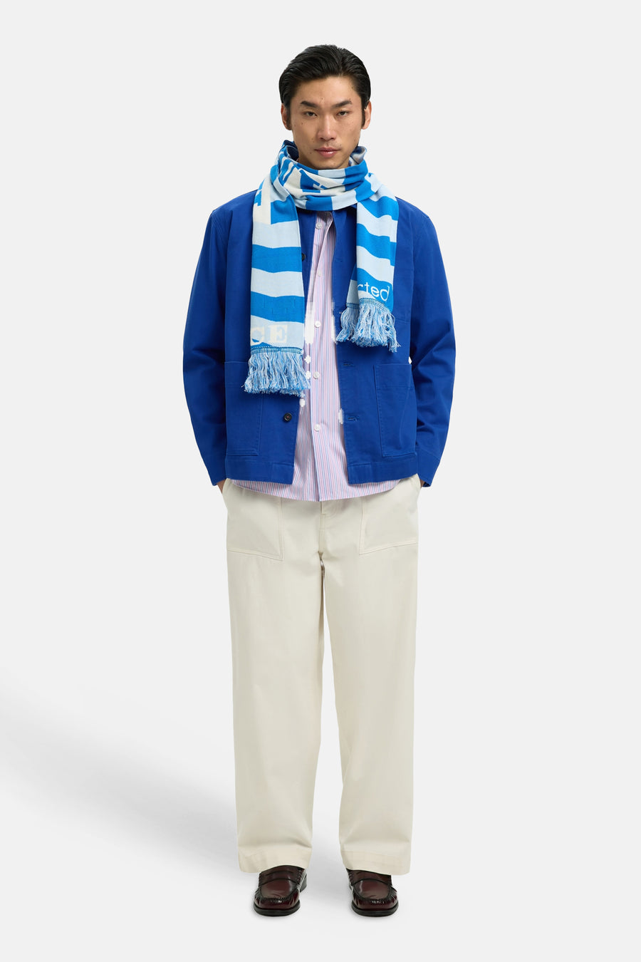 Manteau bleu de SELECTED, porté avec une écharpe rayée et un pantalon beige.