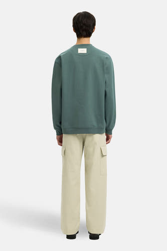 Pull vert avec col rond de SELECTED, avec une étiquette dans le dos et combiné avec un pantalon cargo beige.