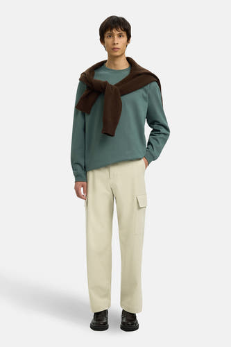 Pull vert de SELECTED à col rond, avec un pull marron noué nonchalamment sur les épaules, porté avec un pantalon cargo crème et des mocassins en cuir.