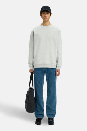 Pull gris de SELECTED, à manches longues, porté avec un jean bleu et une casquette noire.