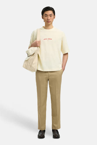 T-shirt écru de SELECTED, avec texte rouge 'Hôtel Amour', porté avec un pantalon kaki, un sac et des mocassins en cuir.