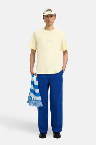 T-shirt à manches courtes écru de SELECTED, avec logo discret sur la poitrine et associé à un pantalon bleu.