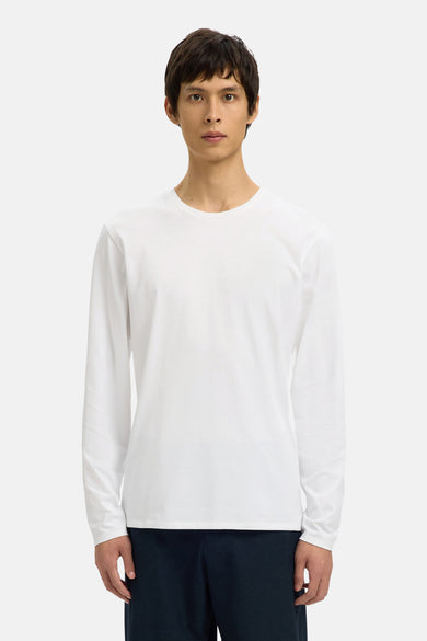 T-shirt blanc à manches longues de SELECTED, porté avec un pantalon foncé, pour un fond neutre.