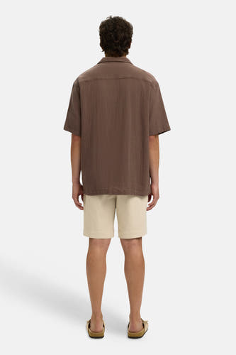 Chemise marron à manches courtes de SELECTED, avec tissu texturé, portée de dos avec un short beige et des sandales marron clair.