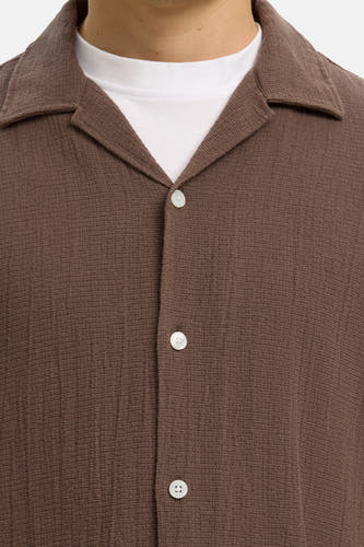 Chemise marron à manches courtes de SELECTED, avec col cubain, tissu texturé et boutons blancs sur un t-shirt blanc.