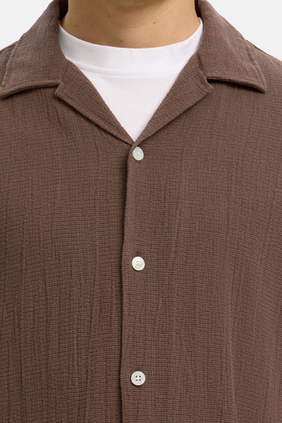 Chemise marron à manches courtes de SELECTED, avec col cubain, tissu texturé et boutons blancs sur un t-shirt blanc.
