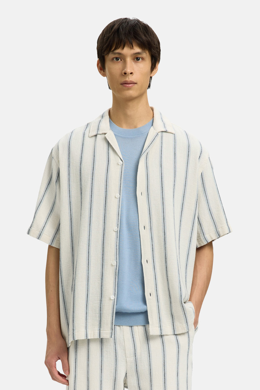 Chemise écru à manches courtes de SELECTED, rayée et portée sur une chemise bleue, avec short et sac assortis.