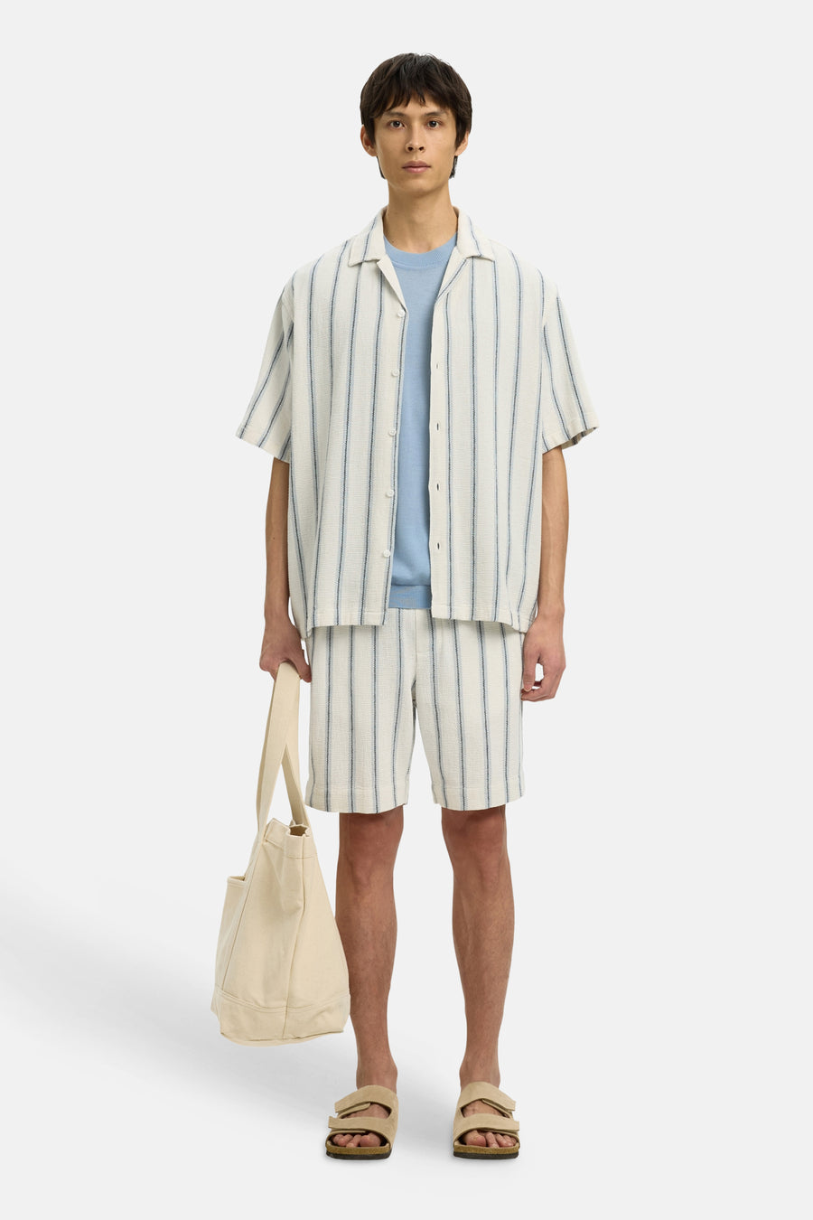 Ecru overhemd met korte mouwen van SELECTED, gestreept en gedragen over een blauw shirt, met bijpassende shorts en tas.
