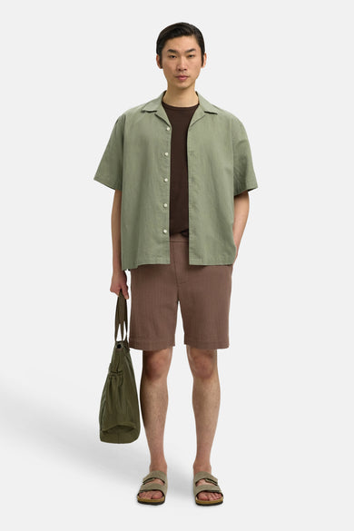 Bruine korte broek van SELECTED met fijne textuur, gedragen met groen overhemd en sandalen, front view.
