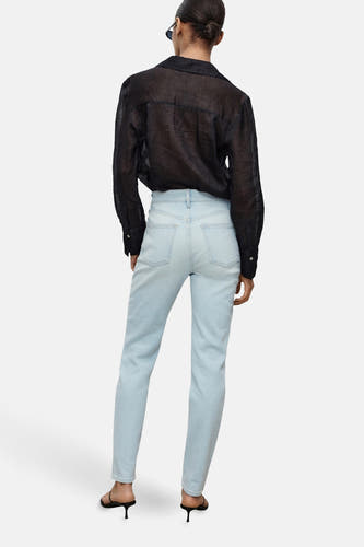 Lichtblauwe mom jeans van MANGO, met hoge taille en achterkant in de schijnwerpers, gecombineerd met een zwarte blouse.
