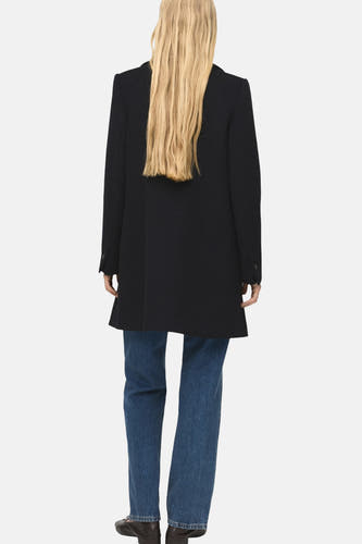 Manteau long noir de MANGO, vu de derrière, avec des jeans bleus et des chaussures noires.