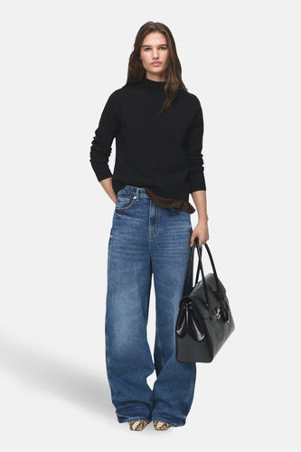 Vrouw met zwarte trui, wijde jeans en zwarte tas.