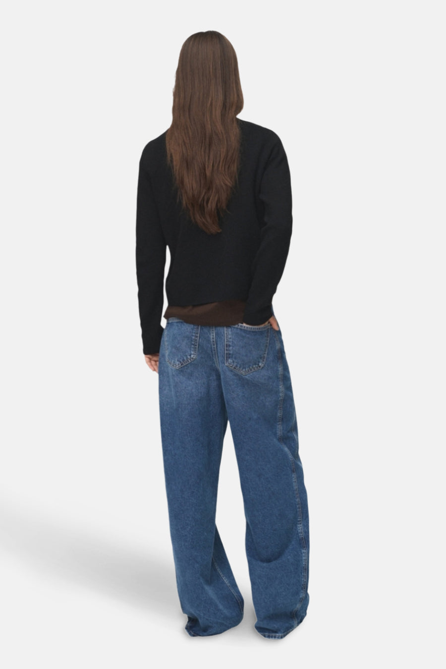 Persoon van achteren, lange bruine haren, zwarte trui, bruin shirt, blauwe wijde jeans.