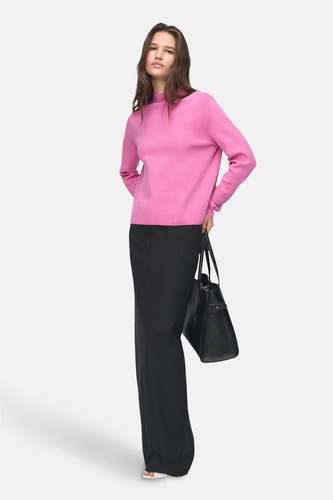 Roze trui met ronde hals van MANGO, gecombineerd met een zwarte, lange broek en een zwarte handtas.