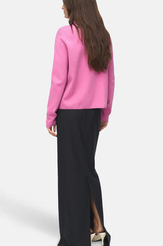 Blouse rose avec col rond de MANGO, vue de derrière avec des manches longues et une longue jupe noire fendue.